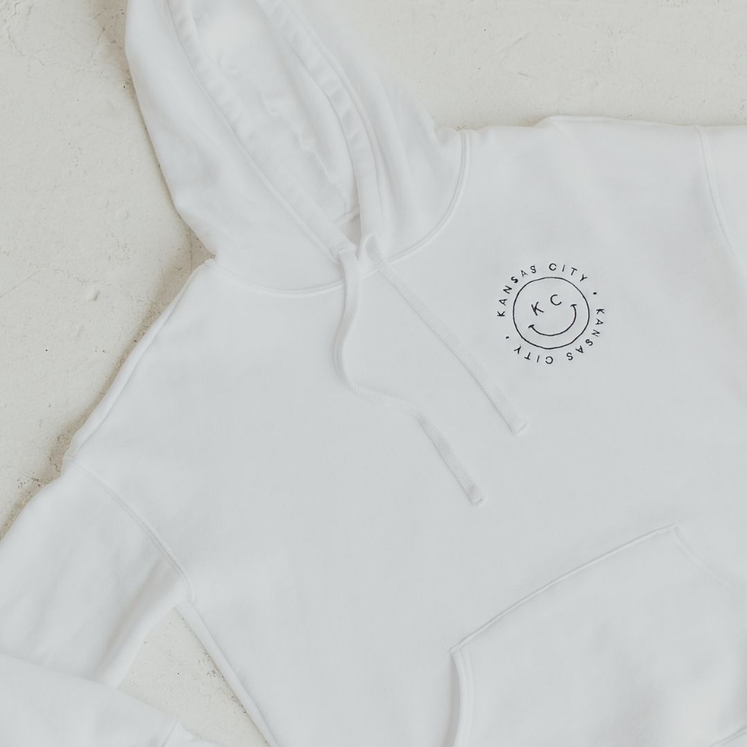 Ready to conquer Monday in style? Start your week with a smile and our comfy KC Smiley Hoodie in white, now available in